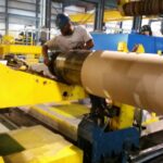 Worker beside a large cylindrical roll or shaft on production equipment