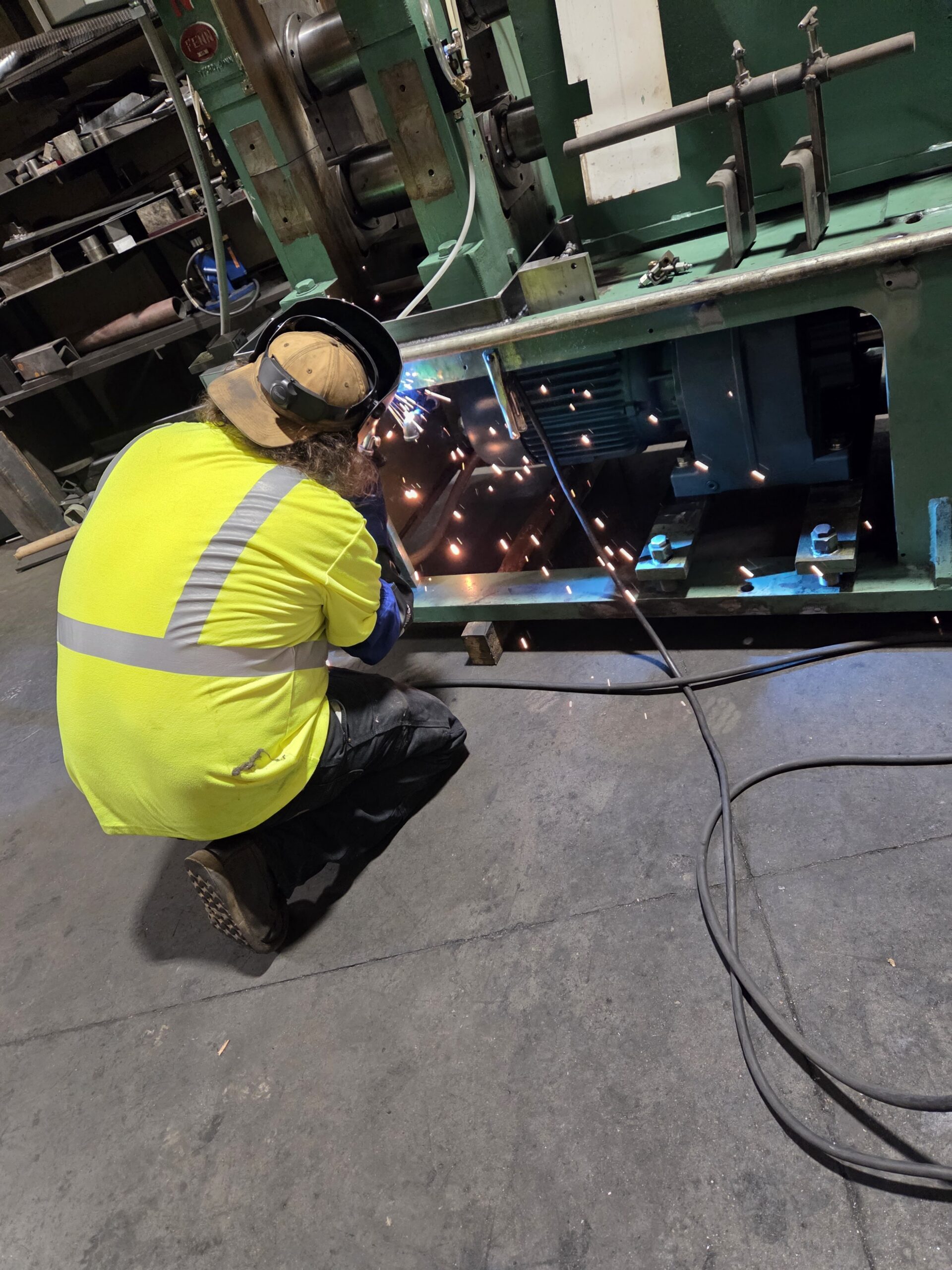 NMS technician welding on industrial production equipment.