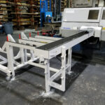 White fabricated material-support table installed at an industrial saw